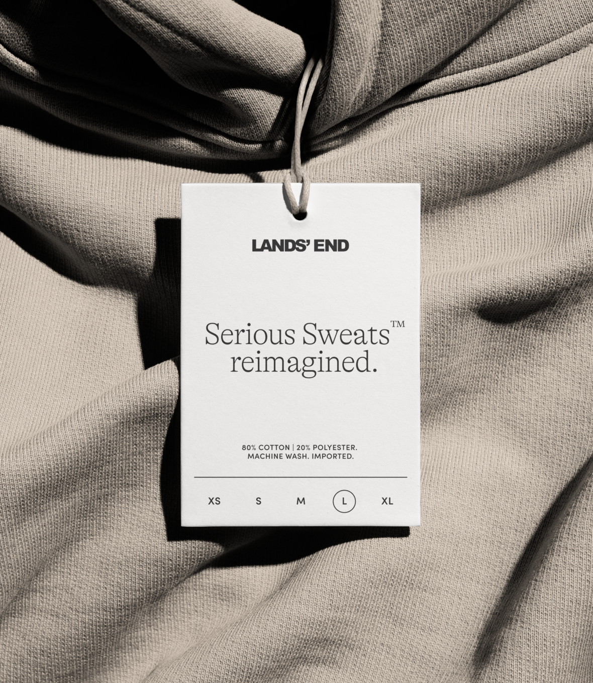Clothing tag showing Lands' End branding with the text "Serious Sweats reimagined" resting on a grey sweatshirt.