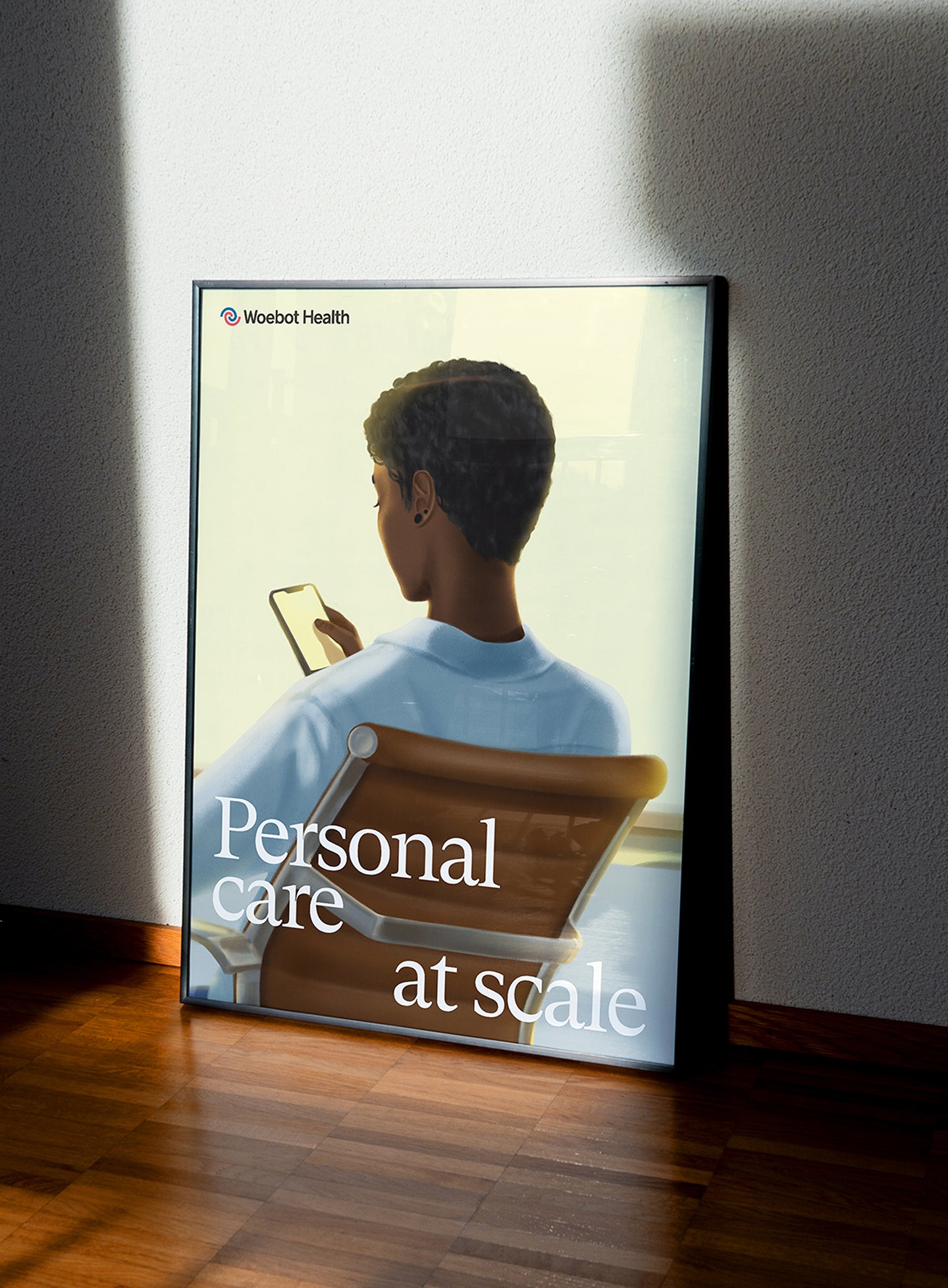 Framed Woebot Health poster leaning against a wall, featuring an illustration of a person sitting in a chair, looking at their phone. The text 'Personal care at scale' is overlaid on the image, emphasizing accessible mental health support.
