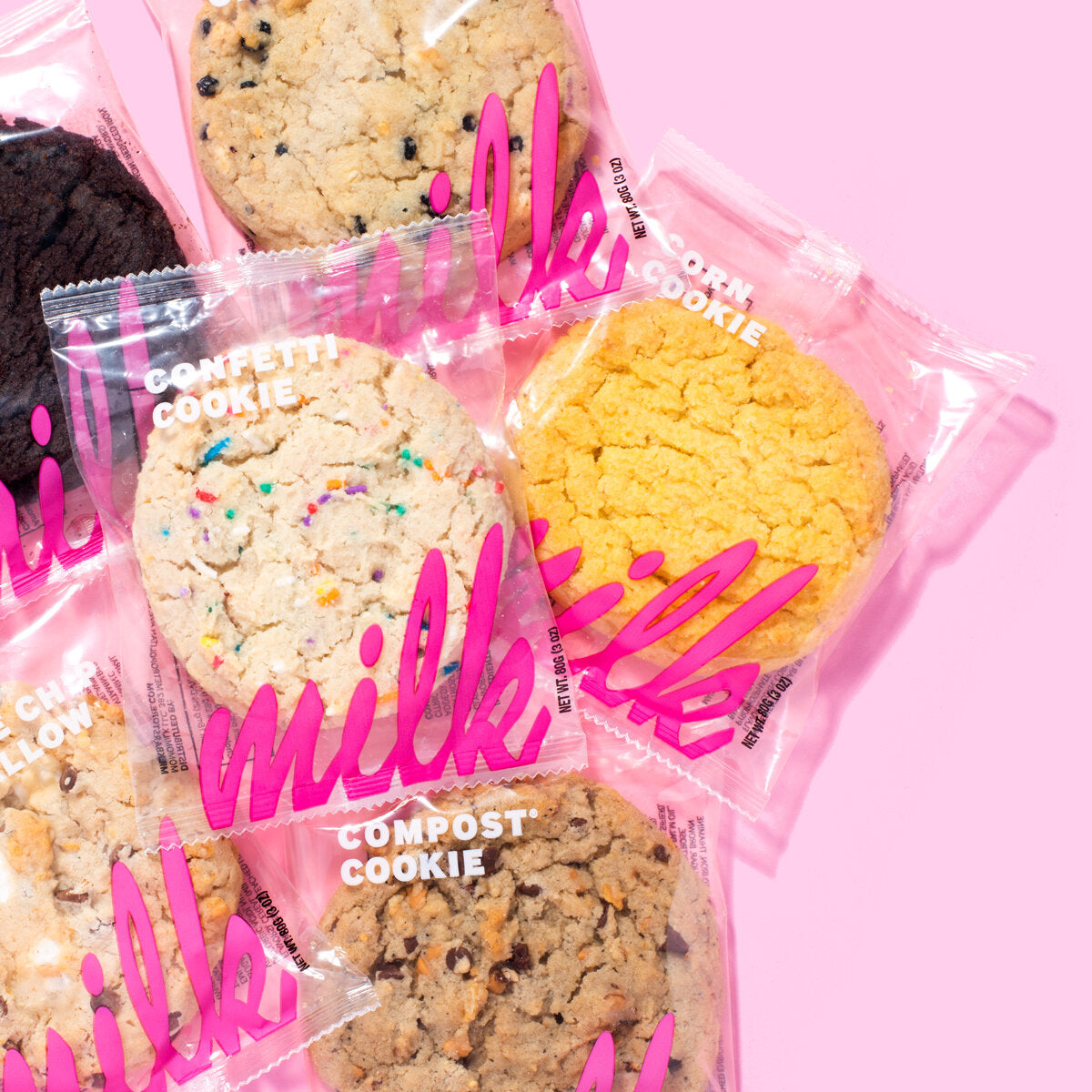 A selection of colorful cookies, including confetti, chocolate chip, and compost cookies, displayed in clear packaging with vibrant pink "milk" branding.