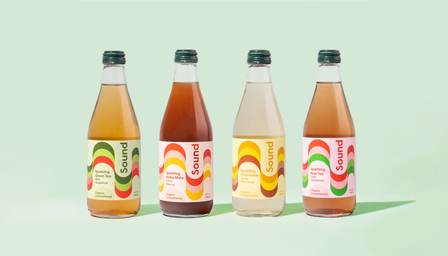 Four Sound sparkling tea bottles displayed in a row against a light green background. Each bottle has a colorful, wavy label featuring different flavors: Sparkling Green Tea with Mint and Grapefruit, Sparkling Yerba Mate with Citrus and Hibiscus, Sparkling Chamomile with Vanilla and Elderflower, and Sparkling Rose Tea with Lime and Cardamom.