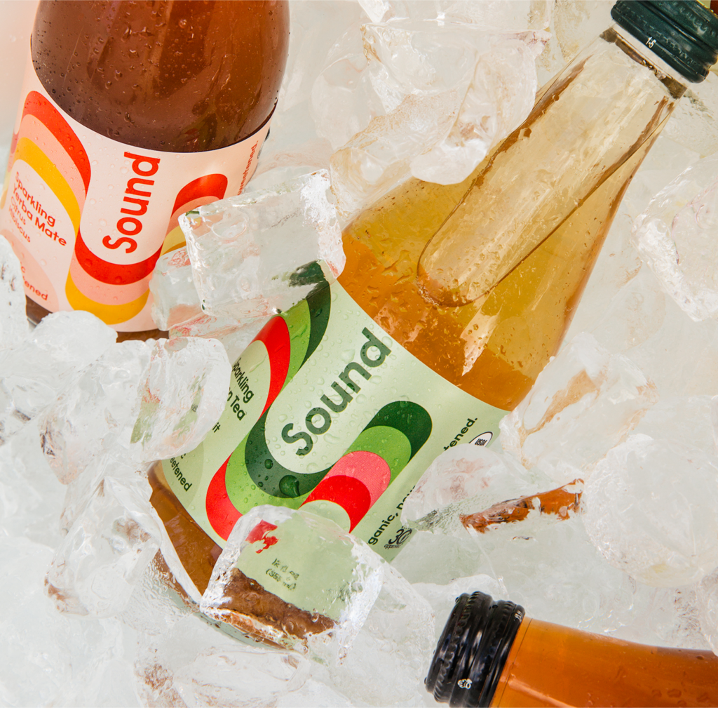 Bottles of Sound sparkling tea are chilled in a bed of ice, with condensation forming on the glass, showcasing their refreshing appeal.