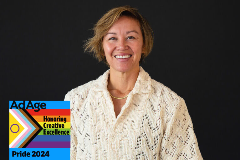 A smiling person wearing a cream-colored textured blouse poses against a black background. A Pride 2024 Ad Age badge in the bottom left corner reads: 'Honoring Creative Excellence.'