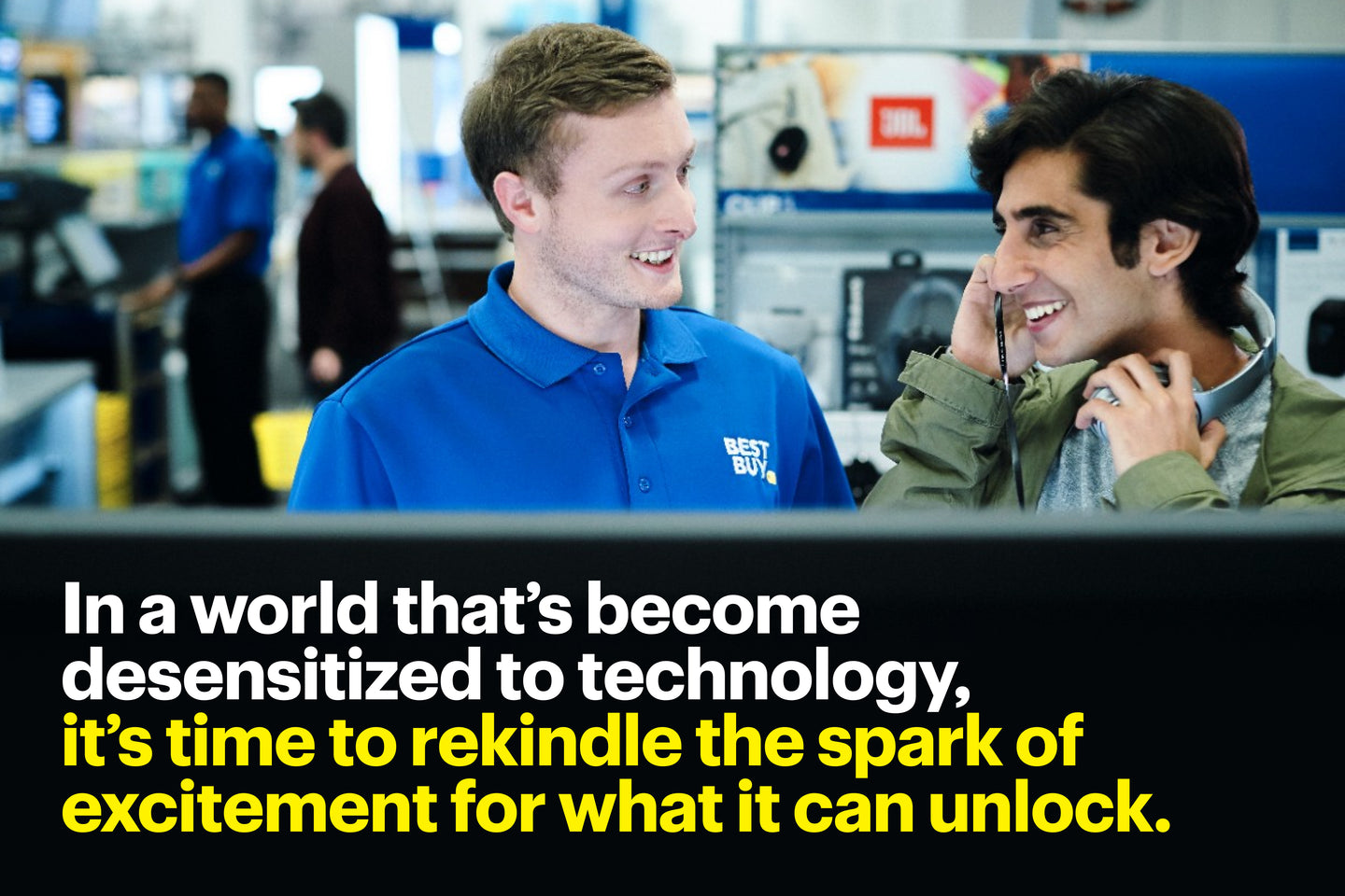 A Best Buy employee in a blue uniform enthusiastically assists a smiling customer trying on headphones in an electronics store. Bold text overlay reads: 'In a world that’s become desensitized to technology, it’s time to rekindle the spark of excitement for what it can unlock.'