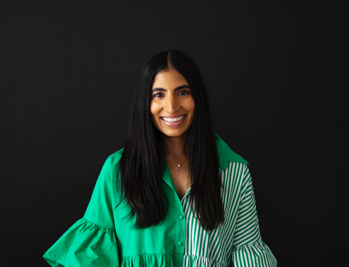 Portrait of a smiling woman with long, straight black hair, wearing a green dress with ruffled sleeves against a black background.